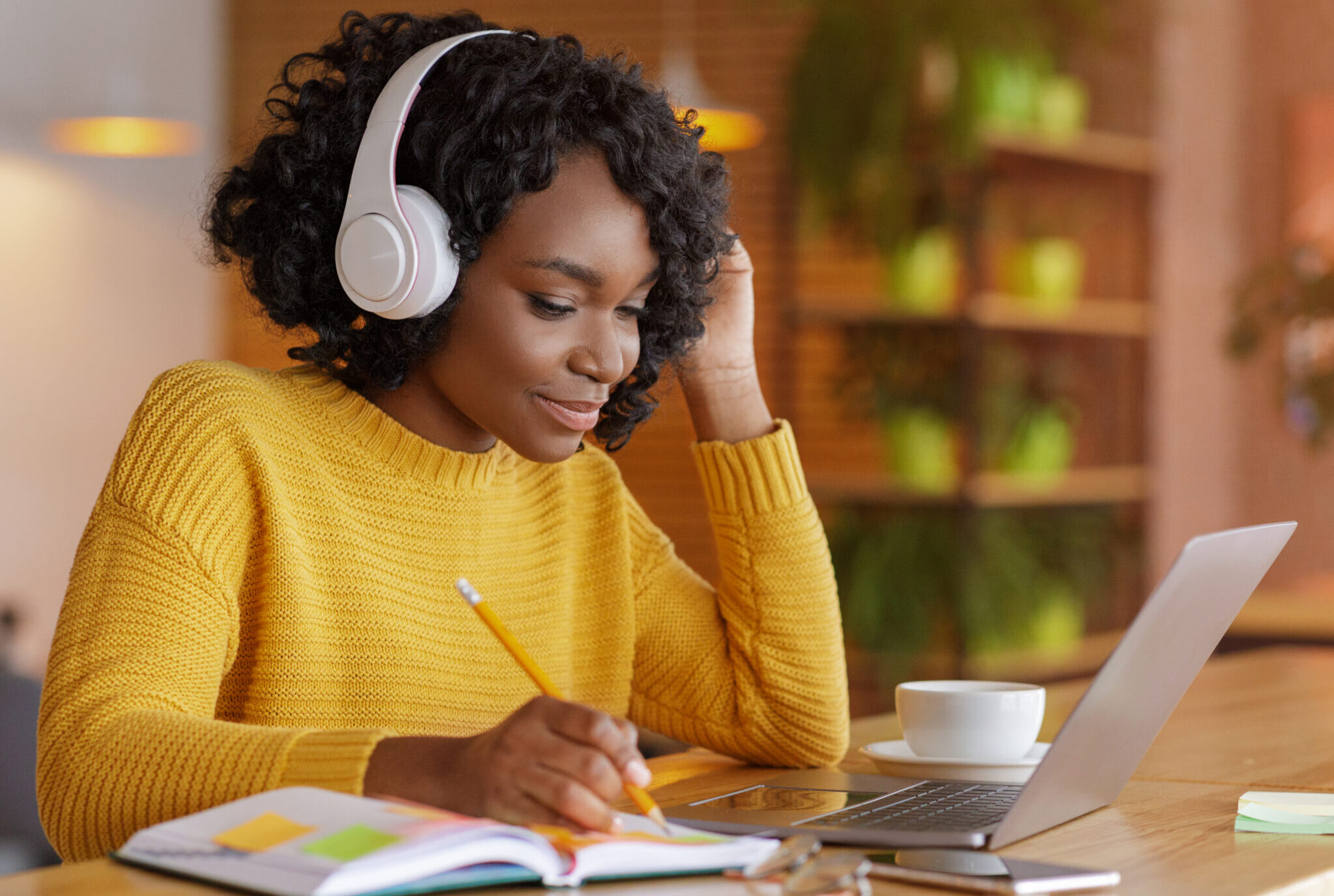 Women working on laptop with headphones in yellow sweater