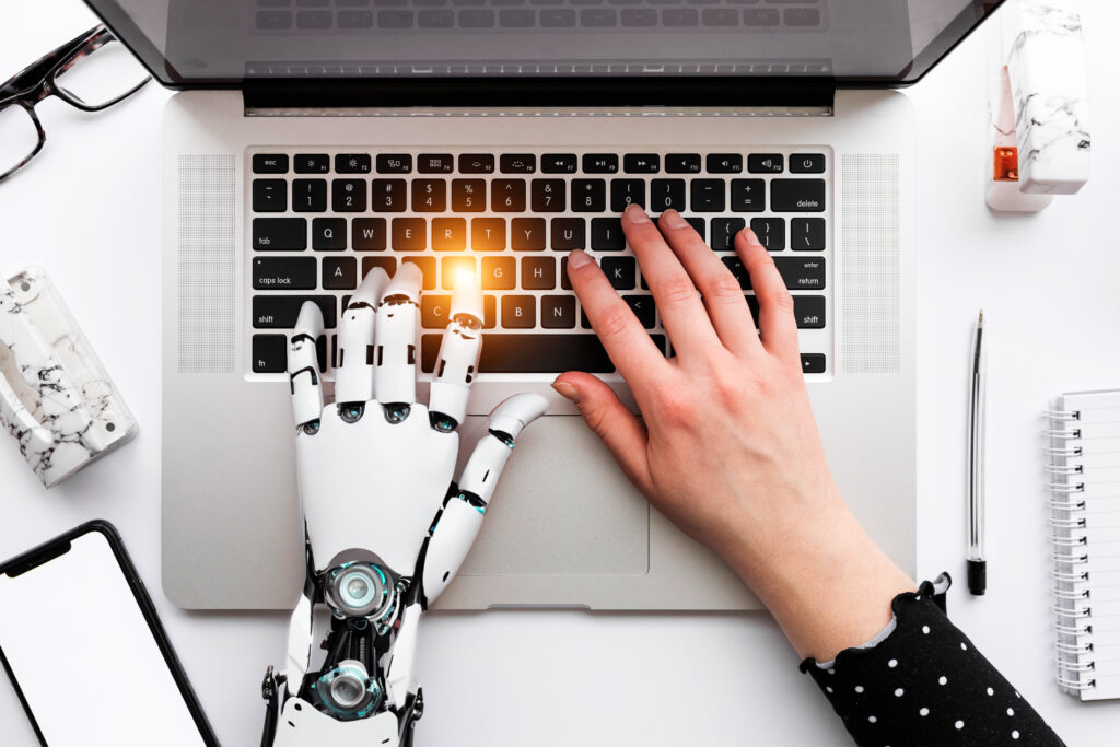 Human hand a robot hand working on a laptop