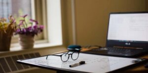 Decorative image of a desk with a laptop, glasses, and office supplies